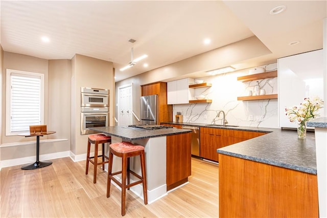 kitchen with sink, appliances with stainless steel finishes, a kitchen breakfast bar, light hardwood / wood-style floors, and decorative backsplash