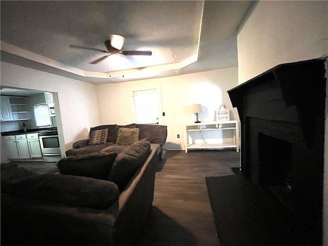 living area featuring a tray ceiling, a fireplace, dark wood-style flooring, and ceiling fan