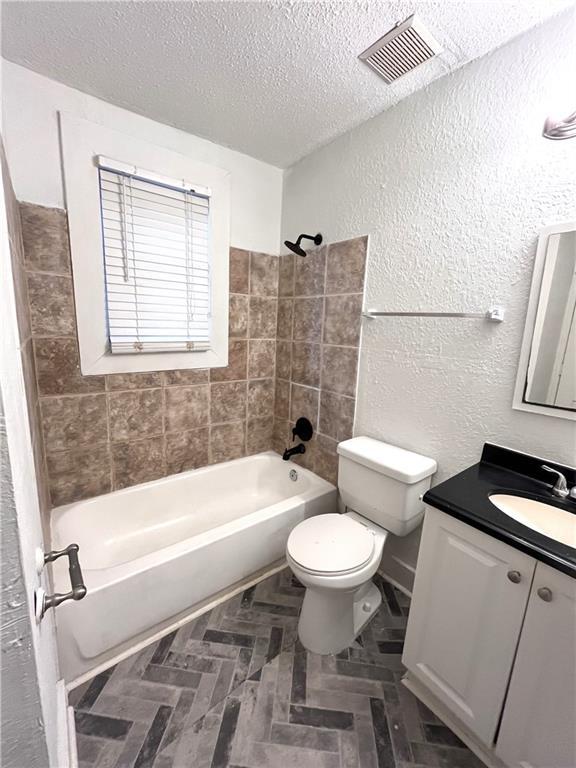 full bathroom featuring visible vents, toilet, a textured ceiling, washtub / shower combination, and a textured wall