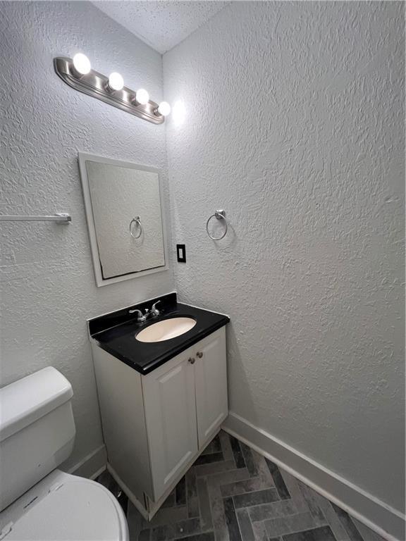 bathroom featuring baseboards, toilet, vanity, and a textured wall