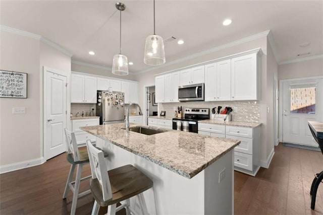 kitchen featuring an island with sink, a sink, appliances with stainless steel finishes, tasteful backsplash, and dark wood-style floors