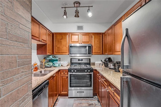 kitchen with visible vents, brown cabinets, a sink, appliances with stainless steel finishes, and light stone countertops
