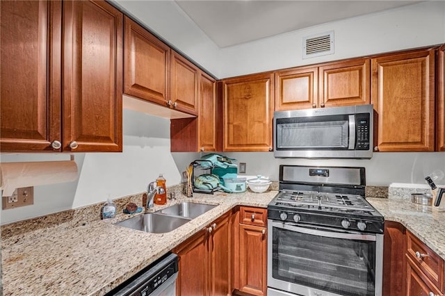 kitchen with light stone countertops, visible vents, a sink, appliances with stainless steel finishes, and brown cabinets
