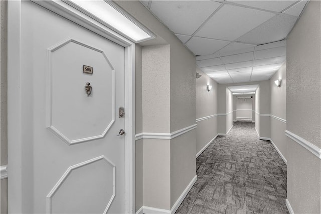 corridor featuring baseboards, a paneled ceiling, carpet, and a textured wall