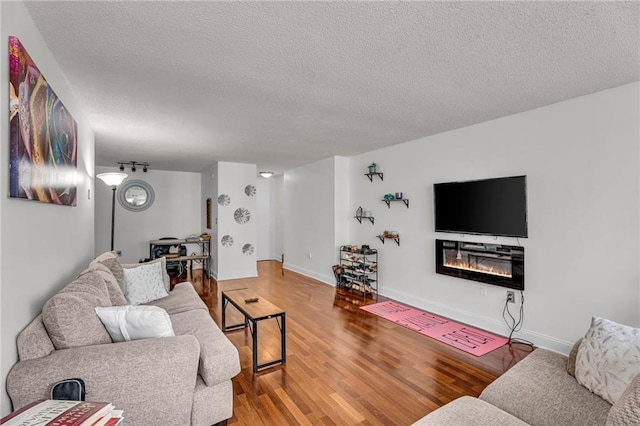living area with a glass covered fireplace, wood finished floors, baseboards, and a textured ceiling