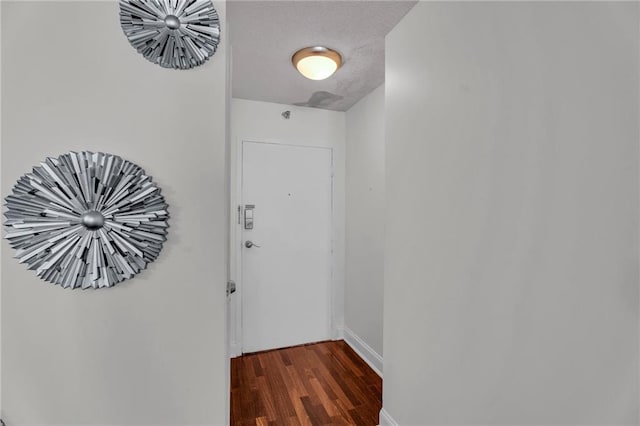 corridor with dark wood-type flooring, baseboards, and a textured ceiling