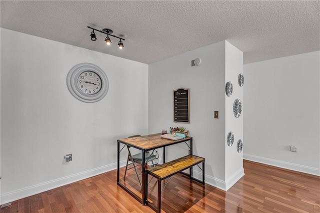 dining area with a textured ceiling, baseboards, and wood finished floors