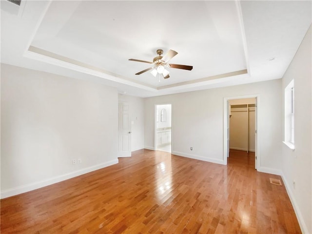 unfurnished room featuring light wood-type flooring, a tray ceiling, and ceiling fan