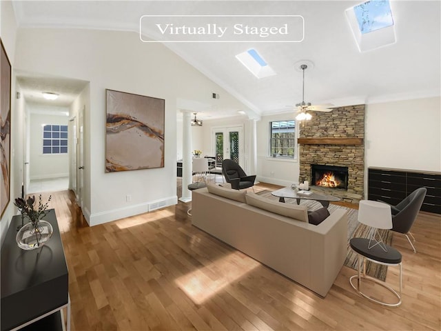 living room with lofted ceiling with skylight, crown molding, ceiling fan, a fireplace, and wood-type flooring