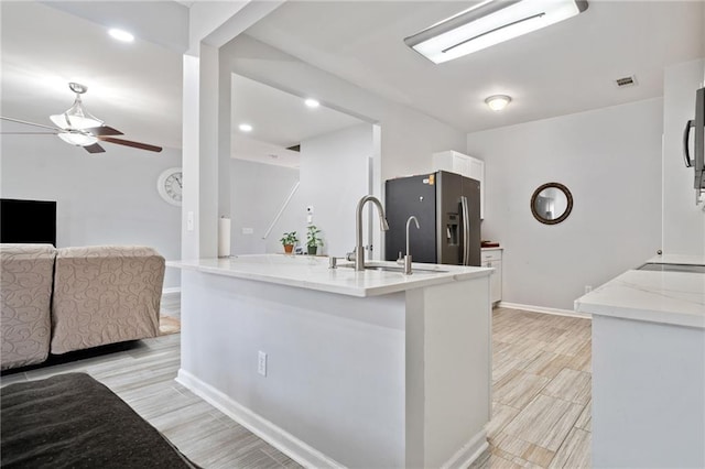 kitchen featuring visible vents, a sink, white cabinetry, stainless steel fridge with ice dispenser, and light stone countertops