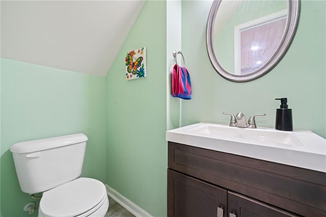 half bathroom with baseboards, toilet, lofted ceiling, wood finished floors, and vanity