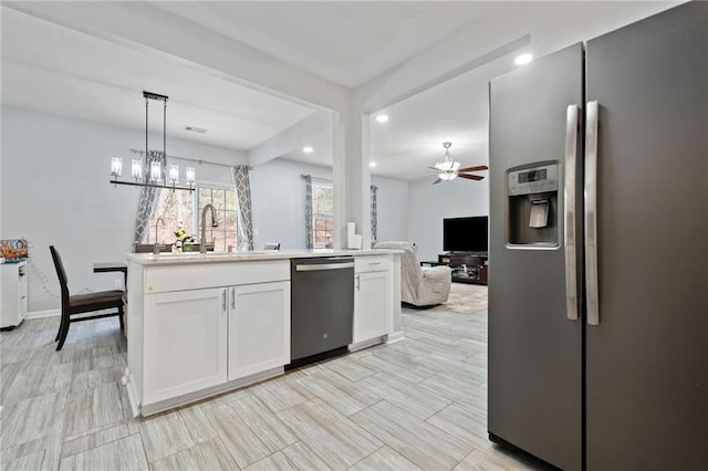 kitchen with ceiling fan with notable chandelier, a sink, open floor plan, appliances with stainless steel finishes, and white cabinets