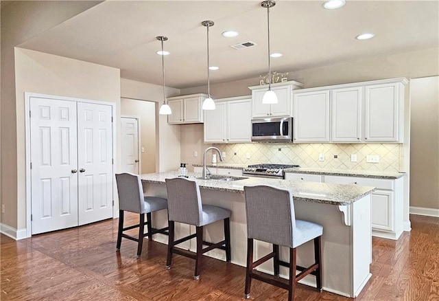 kitchen featuring appliances with stainless steel finishes, a sink, white cabinetry, tasteful backsplash, and dark wood-type flooring