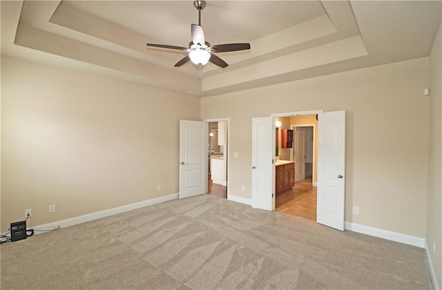 unfurnished bedroom with a tray ceiling, light carpet, baseboards, and connected bathroom