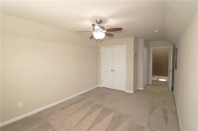 unfurnished bedroom featuring a closet, light colored carpet, baseboards, vaulted ceiling, and a ceiling fan