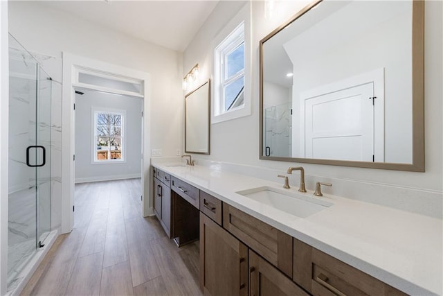bathroom with a marble finish shower, a sink, double vanity, and wood finished floors
