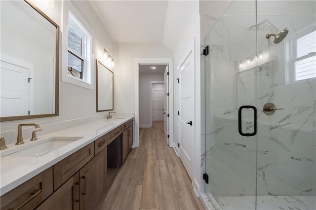 bathroom with double vanity, wood finished floors, a marble finish shower, and a sink