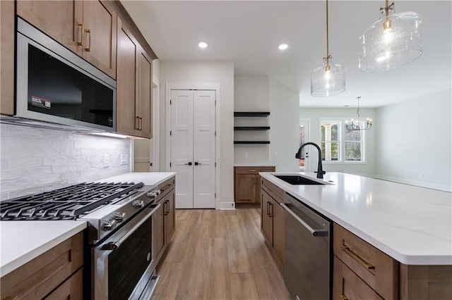kitchen featuring a sink, light wood-style flooring, backsplash, pendant lighting, and appliances with stainless steel finishes
