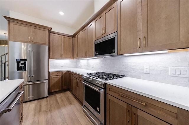 kitchen with light countertops, tasteful backsplash, high end appliances, and light wood-style flooring