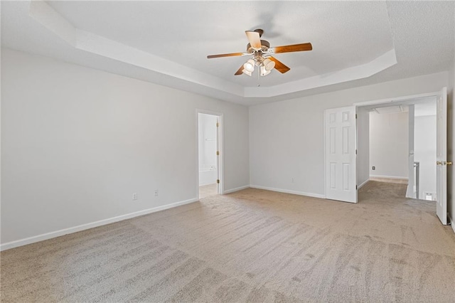 empty room featuring ceiling fan, light colored carpet, and a raised ceiling