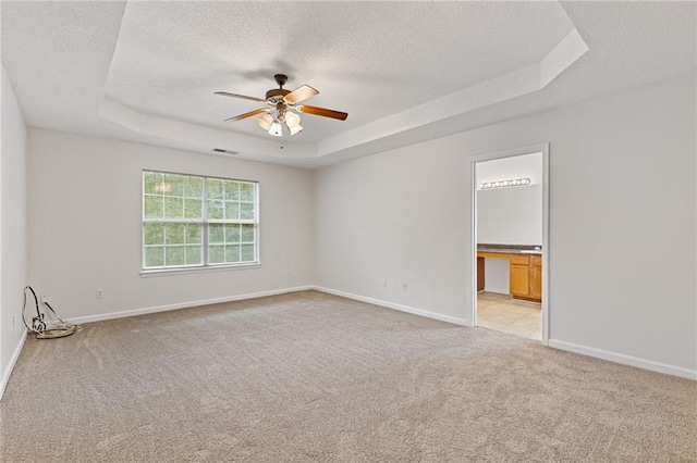 empty room with ceiling fan, a raised ceiling, light carpet, and a textured ceiling