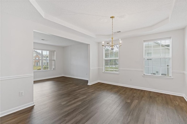 empty room featuring plenty of natural light, a textured ceiling, dark hardwood / wood-style flooring, and a tray ceiling