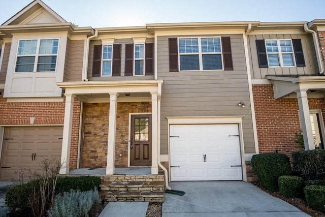 townhome / multi-family property with a garage, stone siding, and concrete driveway