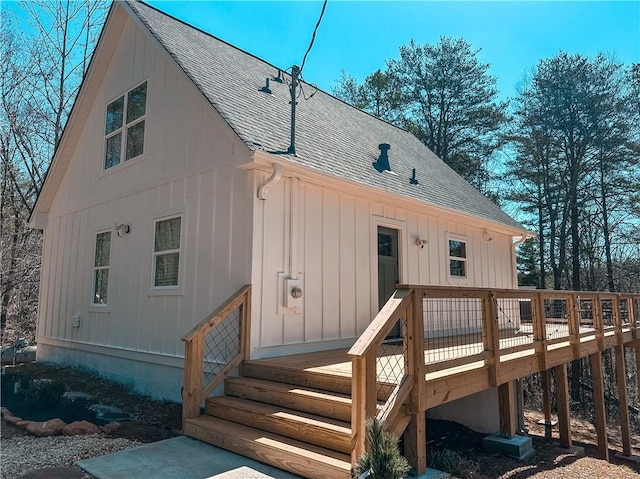 rear view of property with a deck, board and batten siding, and roof with shingles