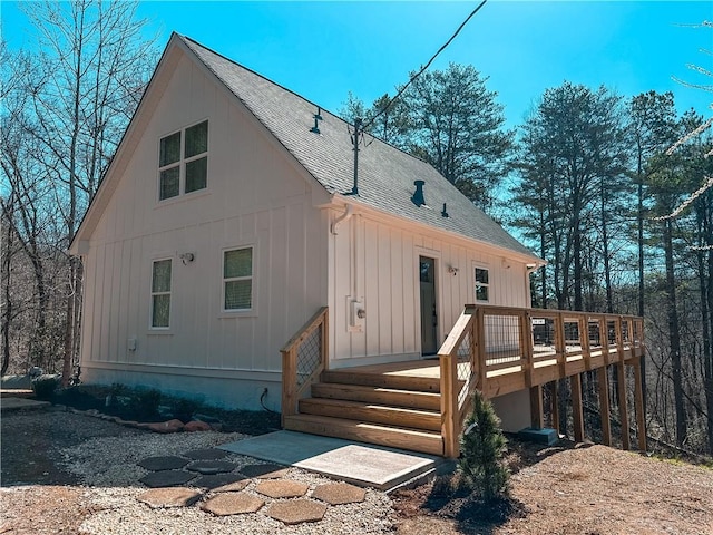 back of property with board and batten siding, a wooden deck, and roof with shingles