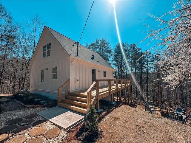 back of property with board and batten siding, a deck, and roof with shingles