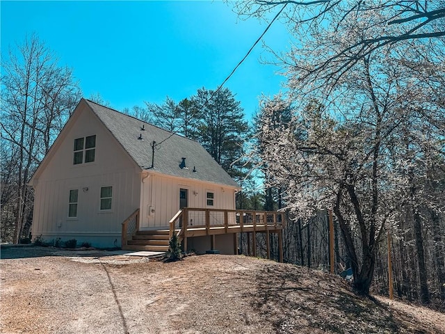 back of house featuring a deck, board and batten siding, and roof with shingles