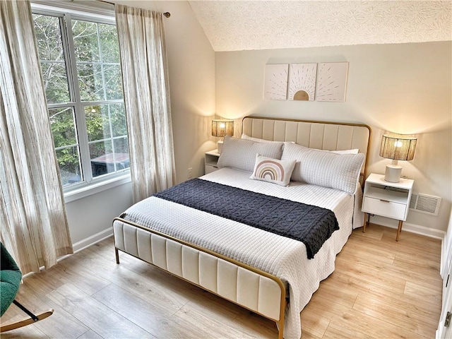 bedroom featuring lofted ceiling, light wood-style floors, baseboards, and a textured ceiling