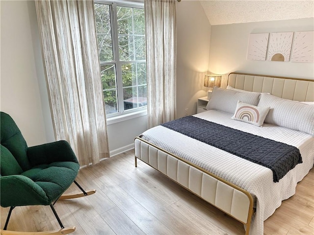 bedroom featuring vaulted ceiling, wood finished floors, baseboards, and a textured ceiling