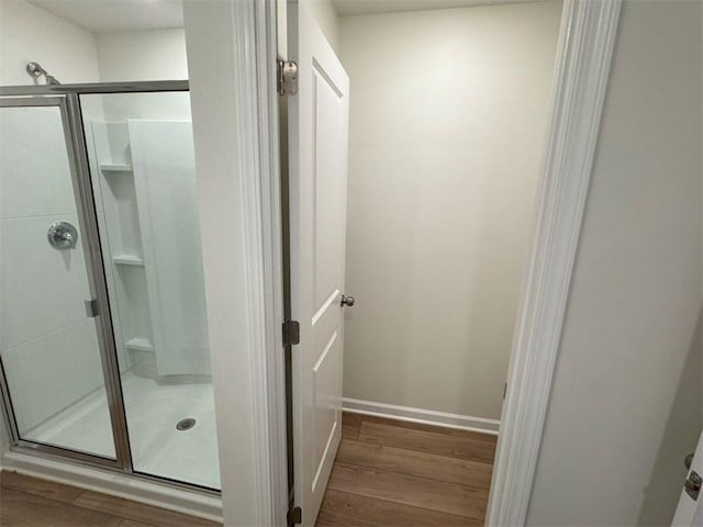 bathroom with a stall shower, wood finished floors, and baseboards