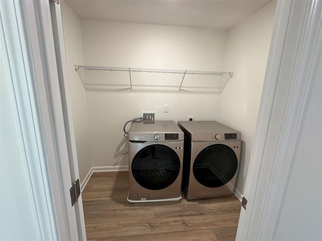 clothes washing area featuring laundry area, baseboards, washer and dryer, and wood finished floors