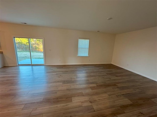 empty room with wood finished floors, visible vents, and baseboards