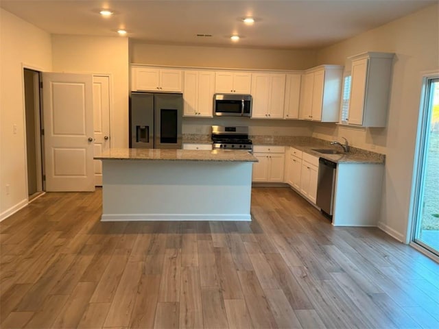 kitchen featuring wood finished floors, a sink, a center island, appliances with stainless steel finishes, and light stone countertops