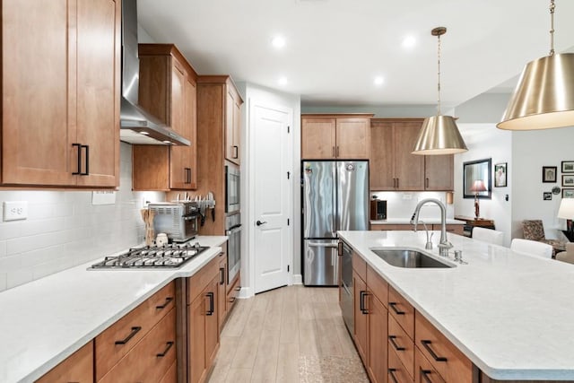 kitchen with appliances with stainless steel finishes, sink, wall chimney range hood, light hardwood / wood-style flooring, and hanging light fixtures