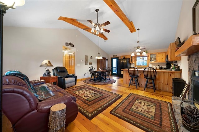 living area with light wood-type flooring, ceiling fan, beamed ceiling, and a stone fireplace