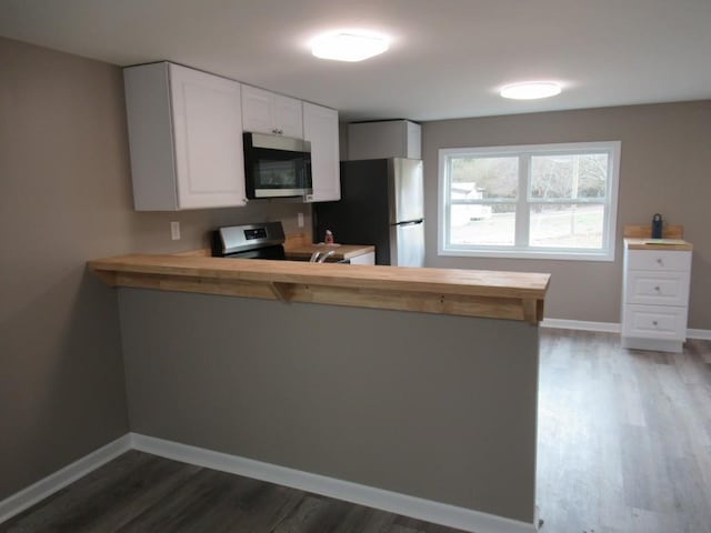 kitchen featuring wooden counters, stainless steel appliances, kitchen peninsula, and white cabinets