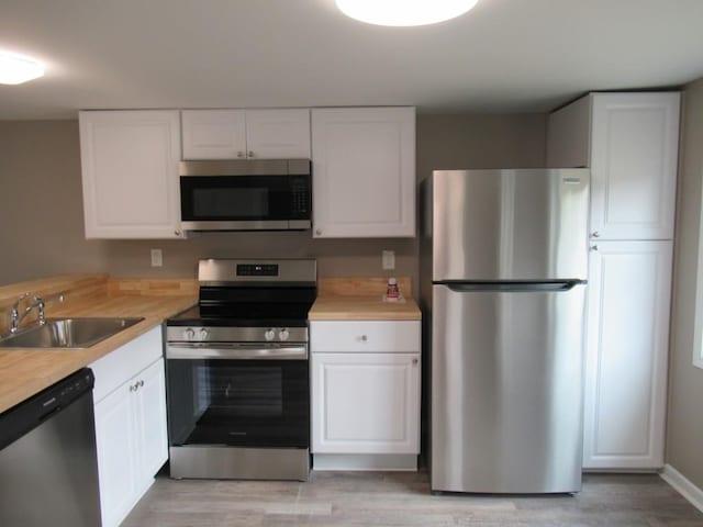 kitchen with wood counters, sink, light hardwood / wood-style flooring, appliances with stainless steel finishes, and white cabinets