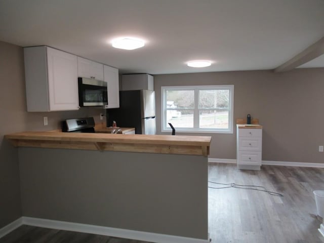 kitchen with stainless steel appliances, white cabinetry, light wood-type flooring, and kitchen peninsula