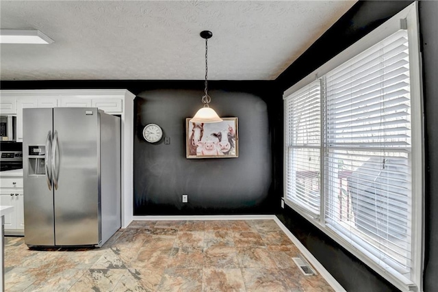 unfurnished dining area featuring stone finish floor, baseboards, visible vents, and a textured ceiling