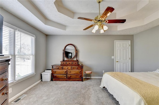 bedroom with a raised ceiling, visible vents, baseboards, and multiple windows