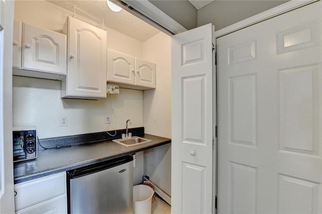 kitchen with stainless steel dishwasher, dark countertops, a sink, and white cabinets