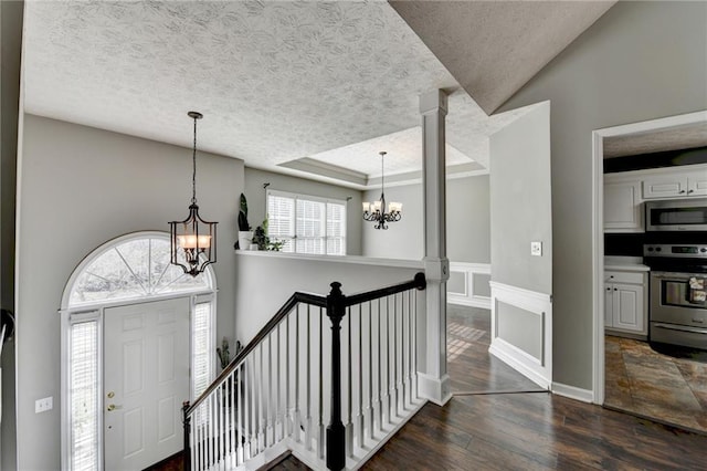 entryway with a chandelier, dark wood-style flooring, a raised ceiling, and a textured ceiling