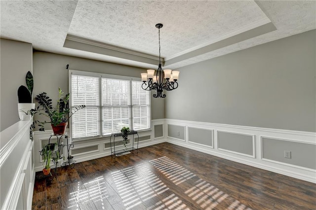 unfurnished dining area featuring a raised ceiling, a textured ceiling, and wood finished floors