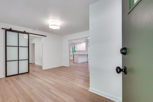 empty room featuring baseboards, light wood finished floors, and a barn door