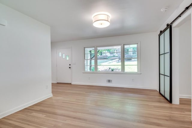 interior space with light wood-style floors, a barn door, visible vents, and baseboards