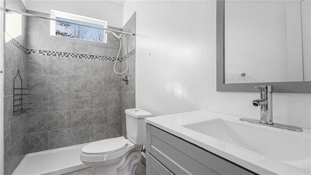 bathroom featuring vanity, a tile shower, and toilet